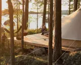 Kloten Nature Resort: en man sitter på en altan vid en sjö, bredvid ett stort tält. En hängmatta och en eldskål syns också.