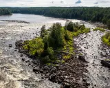 Vattenfall och en träbro över en stenig flod i Kalix, Sverige. Två personer går över bron.