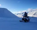 Snöskoterförare i Kebnekaise-området, med snöklädda berg och en klarblå himmel. En känsla av vidsträckthet och äventyr.