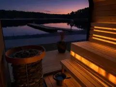 En upplyst bastu i Sverige vid en sjö i skymningen. En vedeldad bastu med stenar och en brygga i bakgrunden.