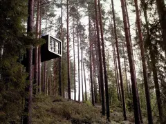 Ett modernt, kubformat rum hänger högt upp bland träden på ett treehotel i Sverige.