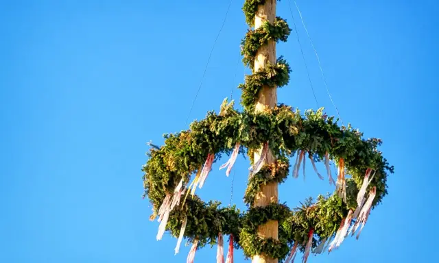 En midsommarstång i Sverige, dekorerad med grönska och band, mot en klarblå himmel.