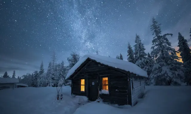 En snöig stuga under en stjärnklar himmel. Det är en perfekt kväll att fotografera vintergatan i Sverige.