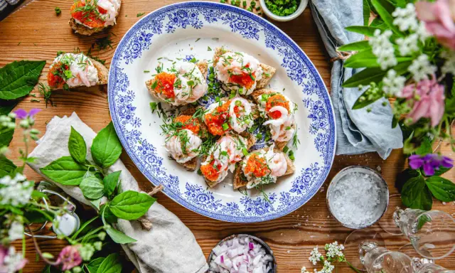 Smörgåsar med räkor och rom, en klassisk svensk midsommar-delikatess, serveras på ett vackert blåvitt fat.