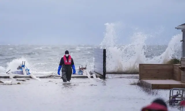 Person i flytväst och stövlar går genom vatten under en storm i Danmark. Vågor slår mot land.