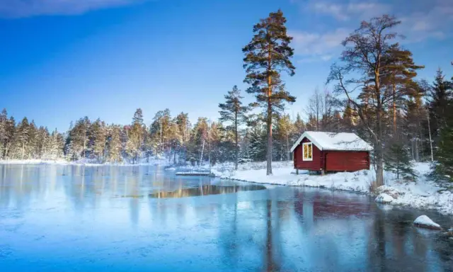 En röd stuga vid en isbelagd sjö i Sverige, perfekt för en mysig julresa.
