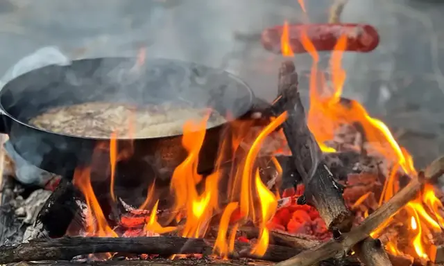 Matlagning över öppen eld, en härlig del av sportlov aktiviteter. Korv och mat i panna över flammande ved.