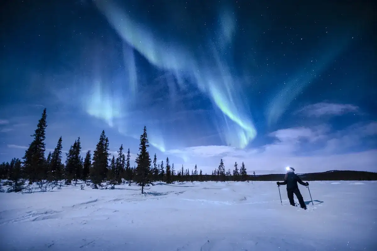 En person med pannlampa och stavar njuter av norrskenet i Swedish Lapland. Besökare ombord på en resa för att uppleva detta magiska skådespel.