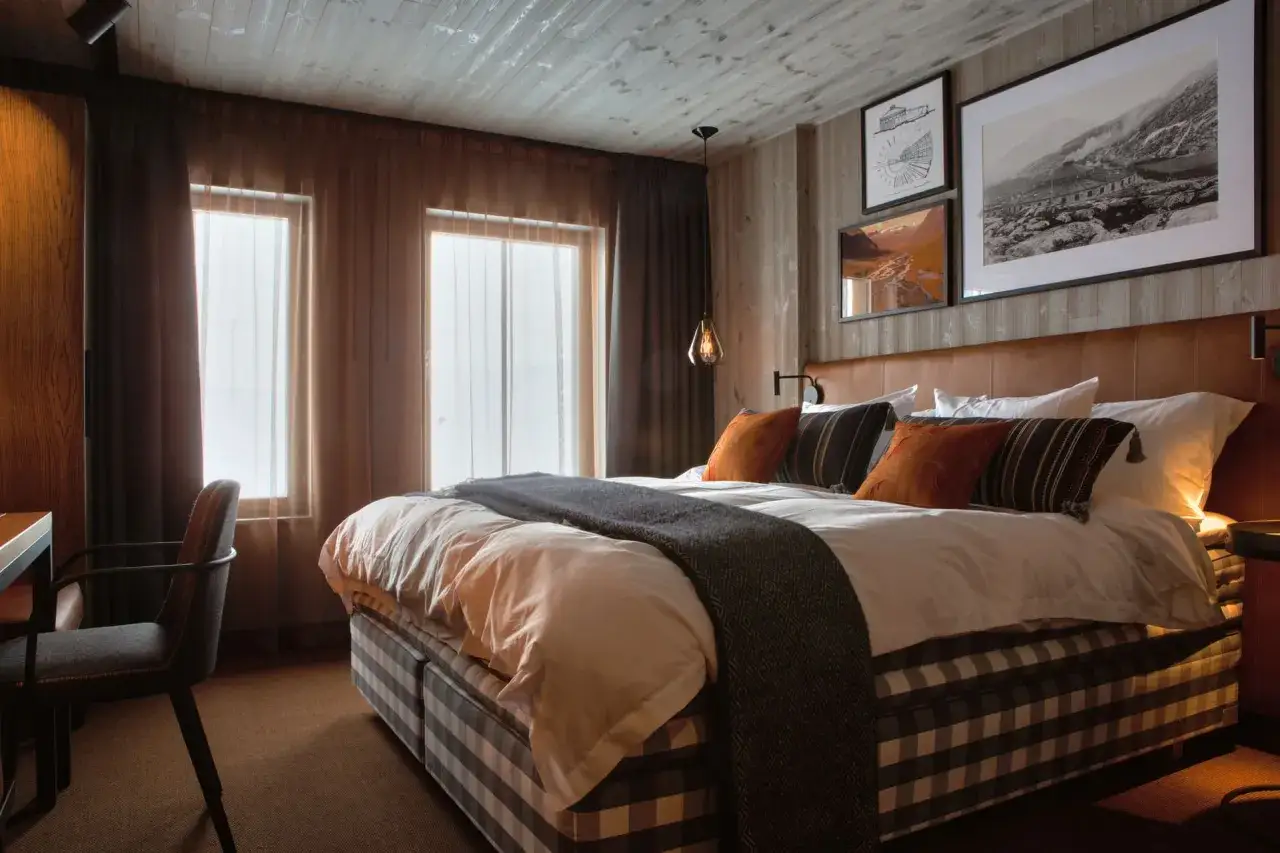 Mysigt sovrum i en niehku mountain villa. En stor säng med rutigt överkast och kuddar i varma färger. Fönster med tunna gardiner.