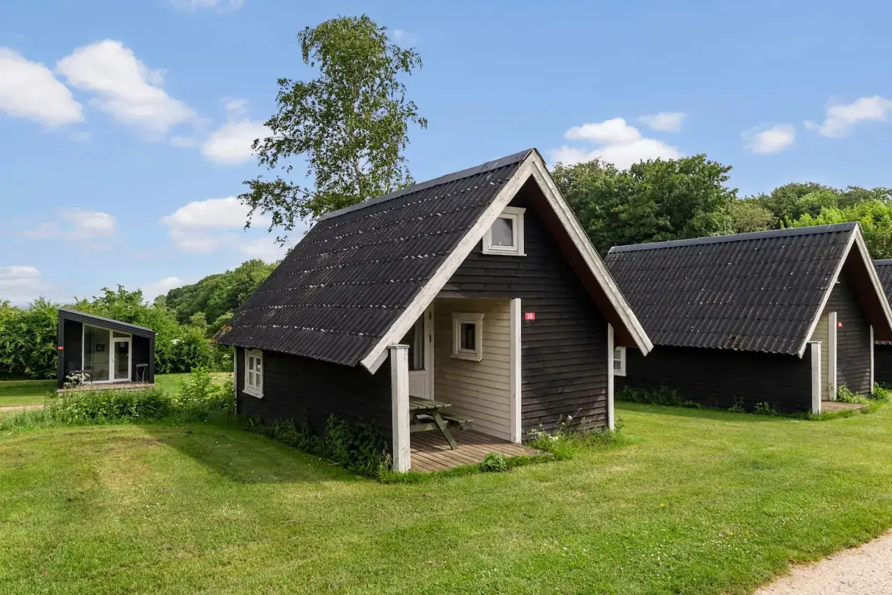 Små, mörka stugor på en grön gräsmatta, perfekt för ditt första camp i Sverige.