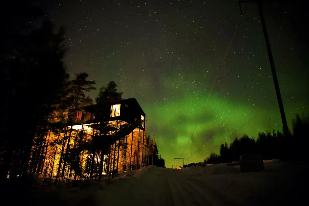 Ett modernt hus i skogen under norrsken, en drömlik vy för swedish lapland visitors board.