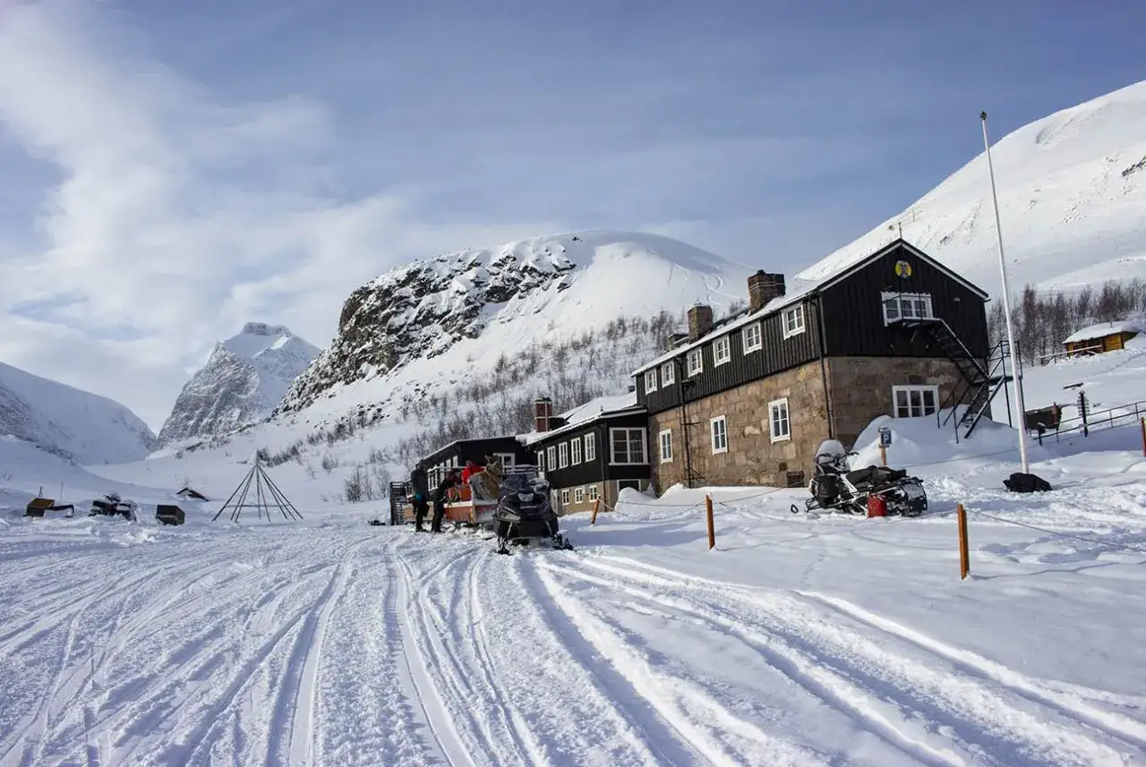 Snöskotrar vid Kebnekaise fjällstation. Vinterlandskap med snöklädda berg och en stor byggnad.