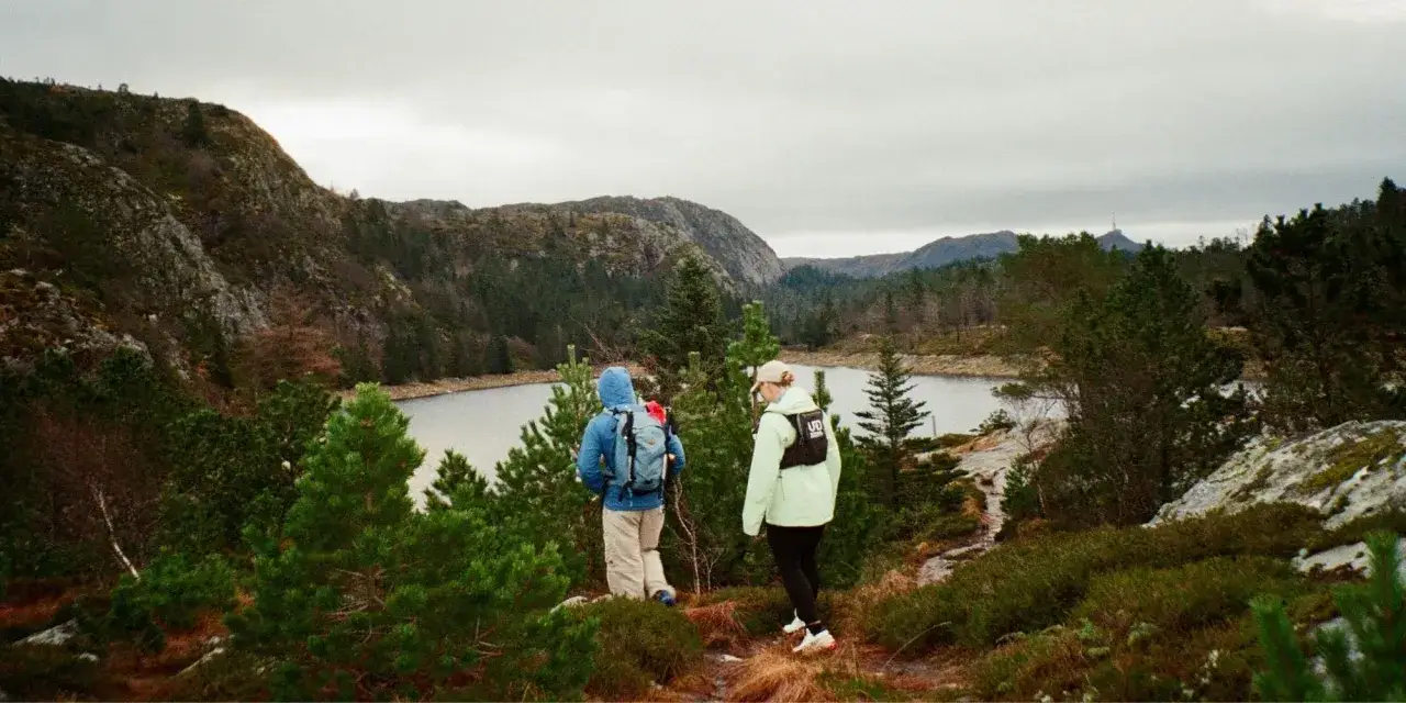 Två personer vandrar på en stig i Sverige, med en sjö och berg i bakgrunden. Fantastiska vandringsleder Sverige.