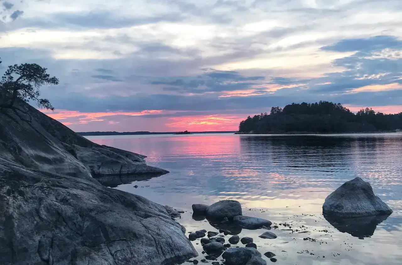 Solnedgång vid Grinda, Stockholms skärgård. Klippor och vatten speglar den rosa himlen.