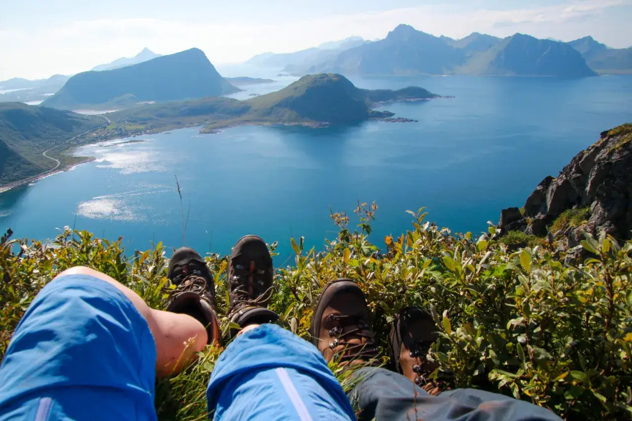 Vandring i Lofoten med fantastisk utsikt över fjordar och berg. Vandrare vilar fötterna bland grönska.