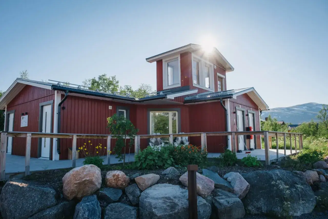 Rött hus med vita knutar och en solig veranda. Abisko Turiststation, redo för äventyr i fjällen.