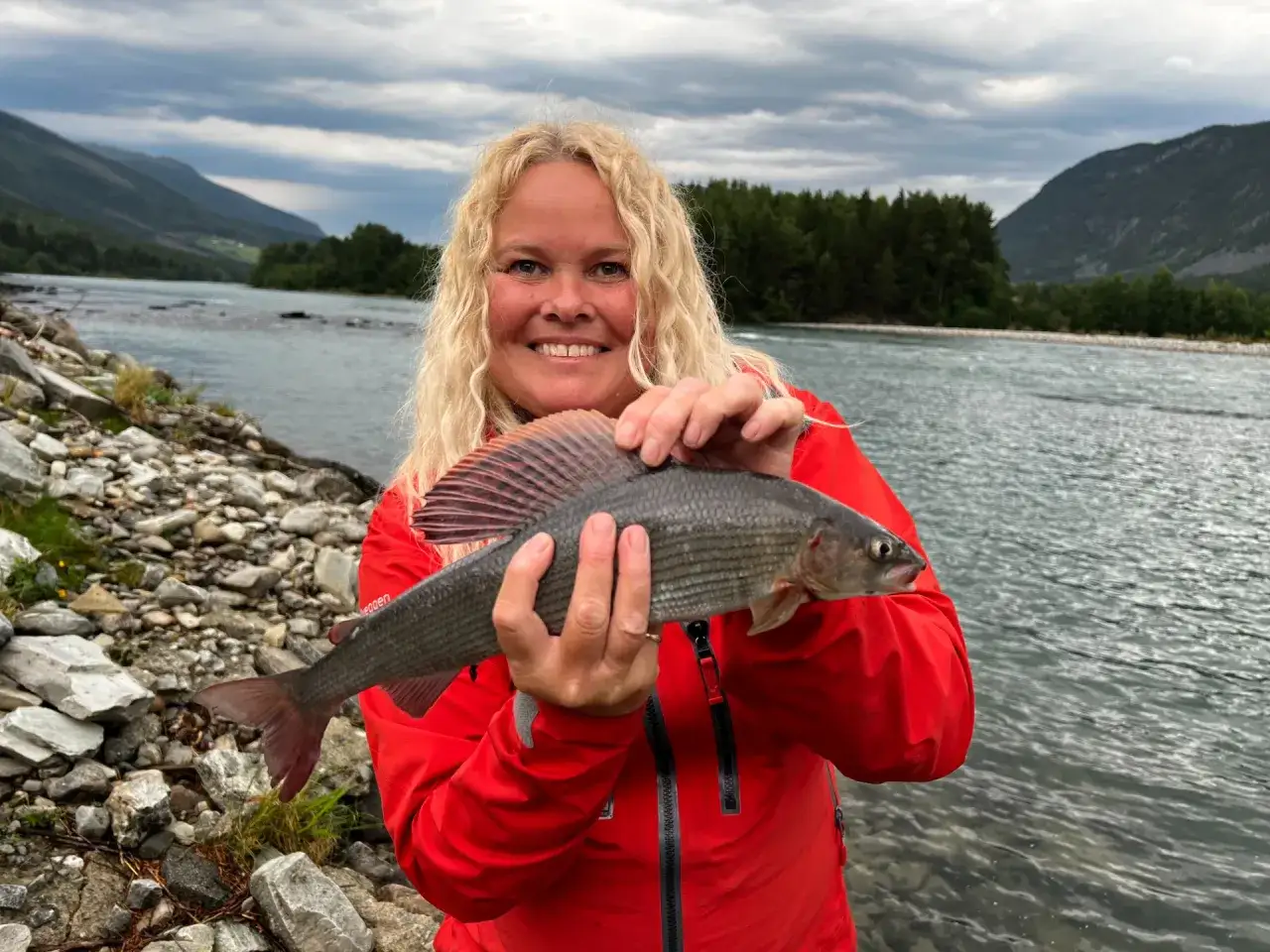 Glad kvinna med en fin fångst vid en älv. En härlig dag för fiska i Sverige.