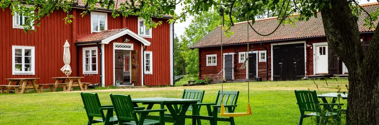 Röda trähus med vita knutar, grönskande gräsmatta och sittgrupper. Ett mysigt stf vandrarhem redo för gäster.
