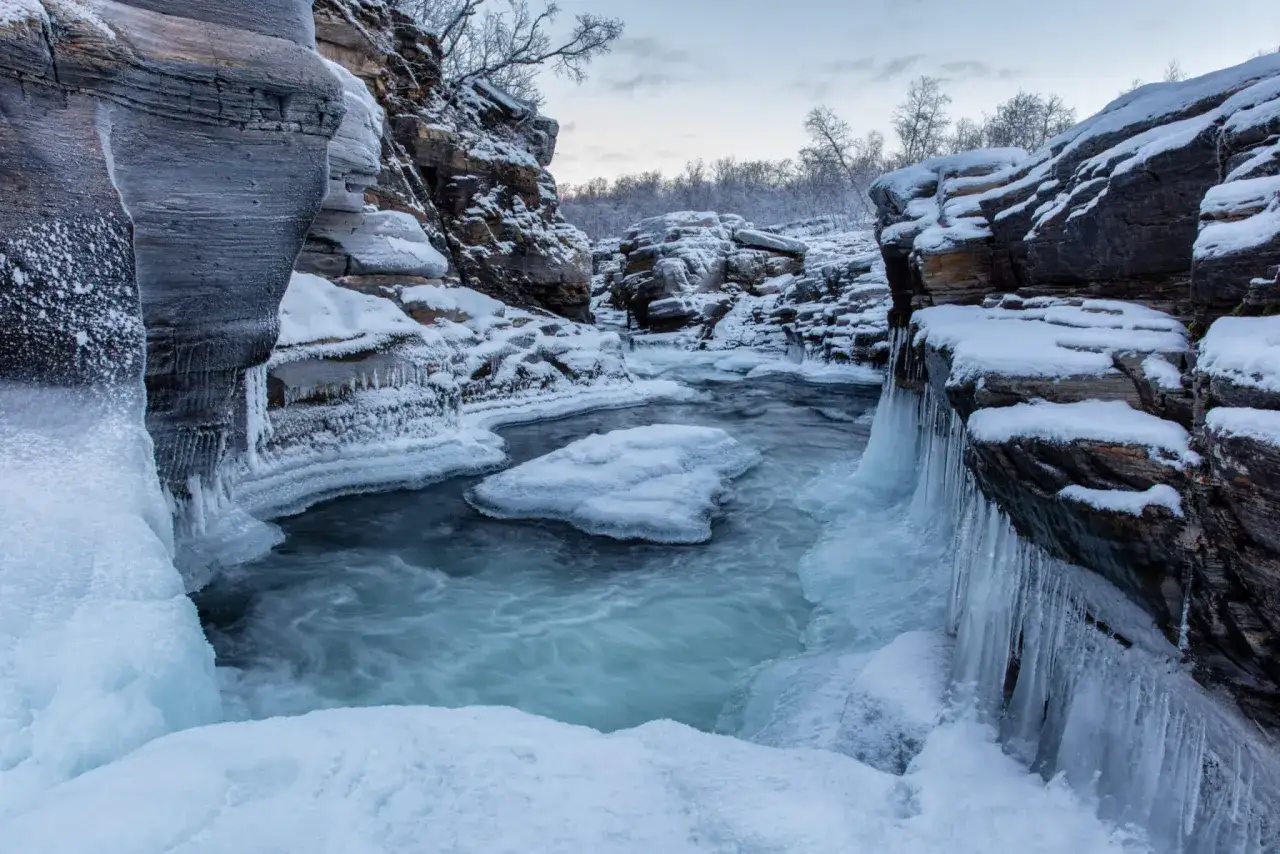 Vinterlandskap i Abisko kanjon med isiga klippor och porlande vatten.