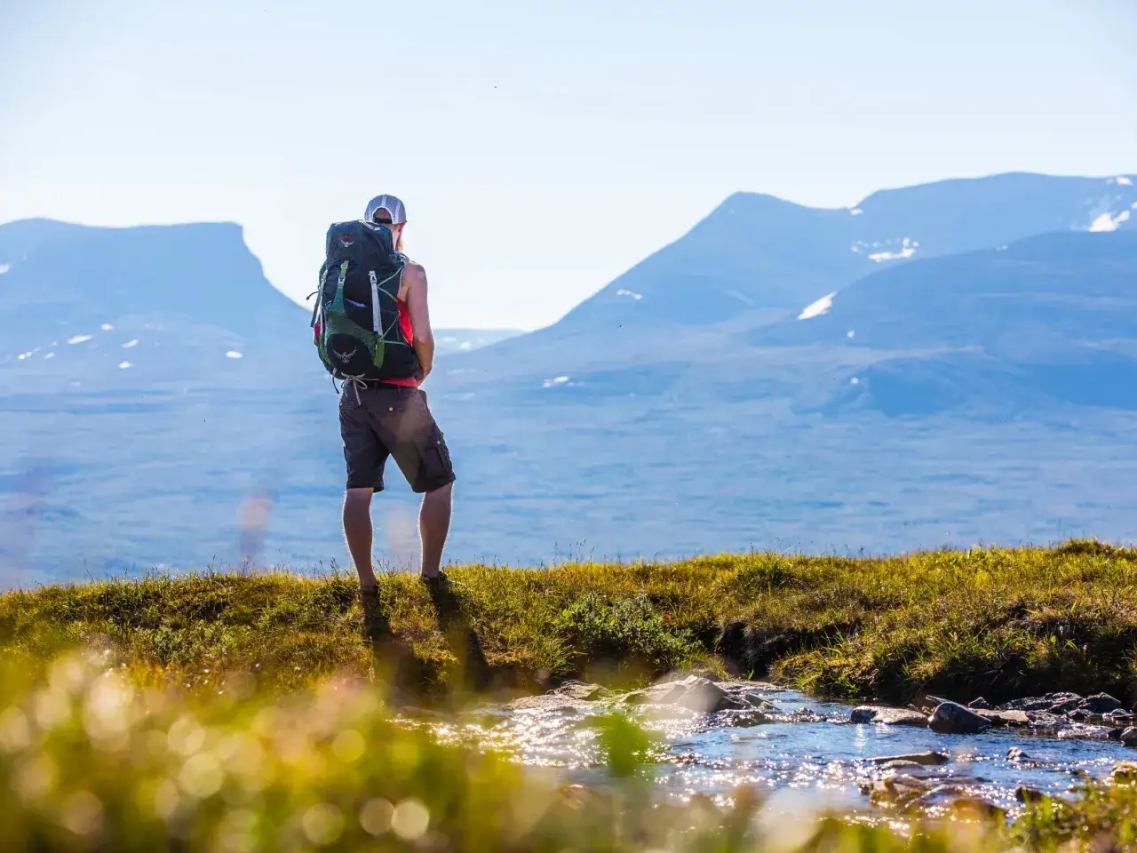 Vandrare med ryggsäck njuter av utsikten över fjällen under en abisko vandring dagstur. En bäck porlar i förgrunden.