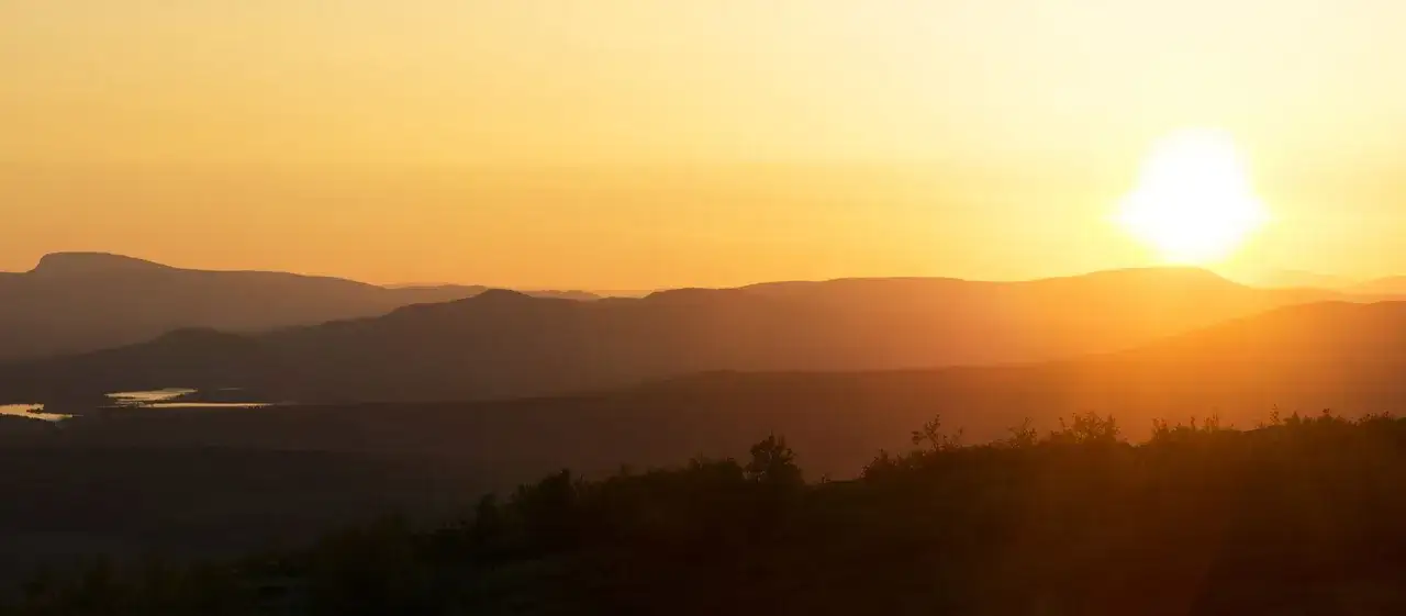 Solnedgång över fjällandskap, en spegelblank sjö i fjärran. En magisk sommar i Sverige.