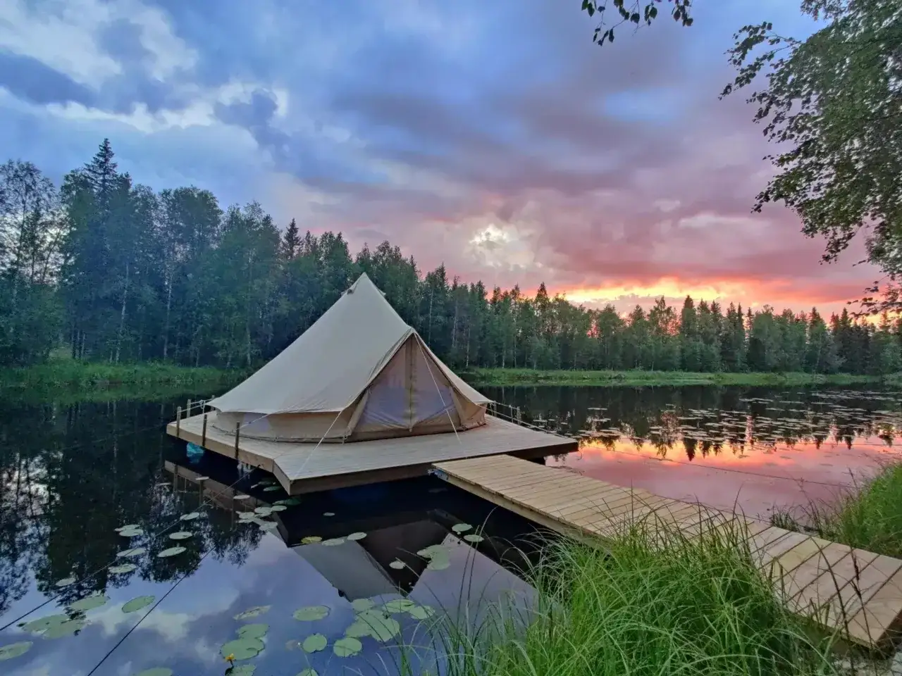 En glampingtält på en flytande plattform i en sjö, med en träbrygga och en vacker solnedgång i Norrbotten.