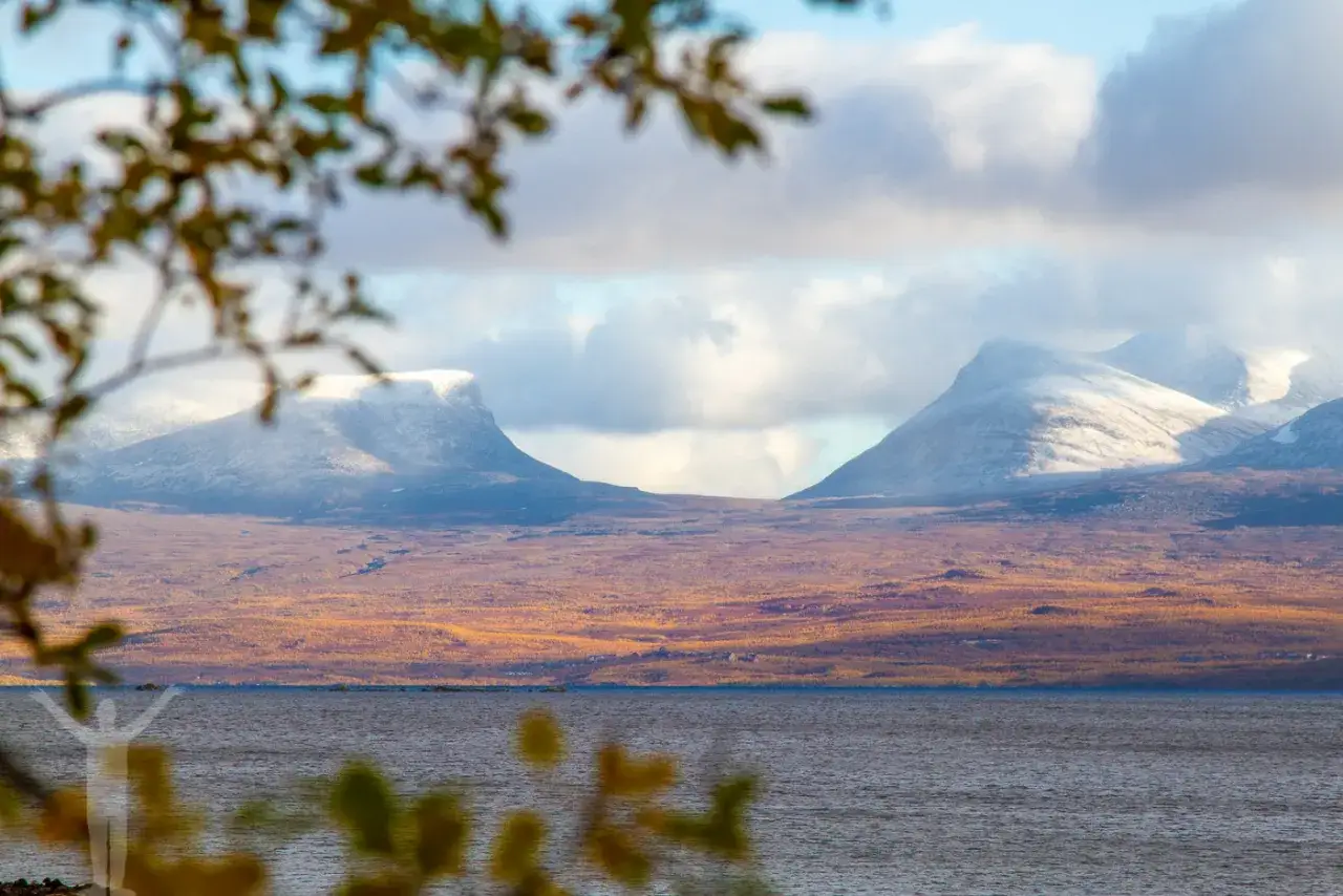Vacker vy över Lapporten i Abisko, Sverige. Snöklädda berg reser sig över en gyllene fjällsluttning vid en sjö.