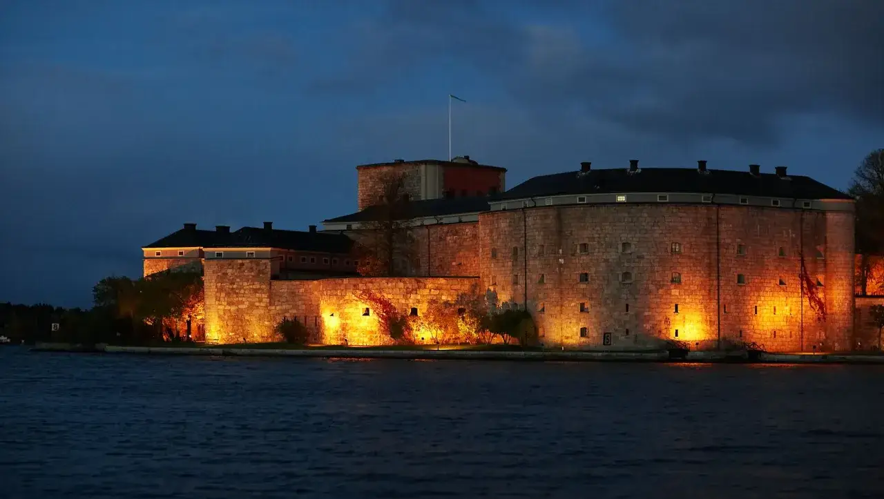 Vaxholms kastell badar i kvällsljus vid vattnet. En historisk fästning som lyser upp mörkret.