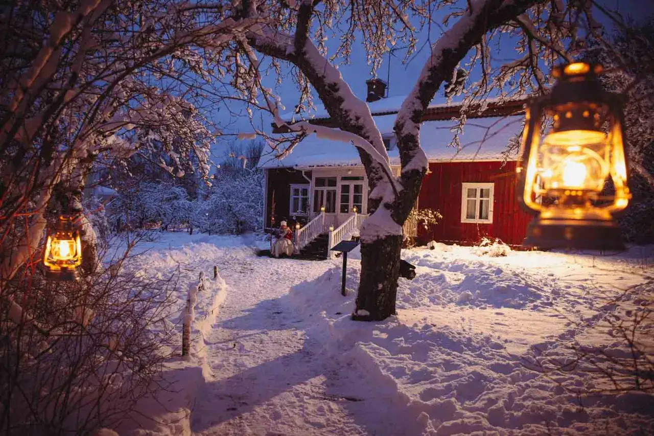 En snöig julresa i Sverige. Ljuslyktor lyser upp en röd stuga med snöklädda träd.