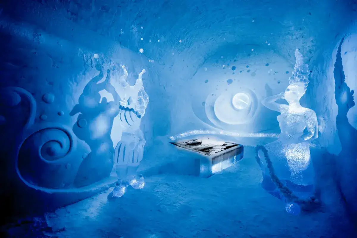 Isstatyett av en figur med en spiralformad bakgrund och en annan figur som en sjöjungfru i ett rum i ice hotel sweden.
