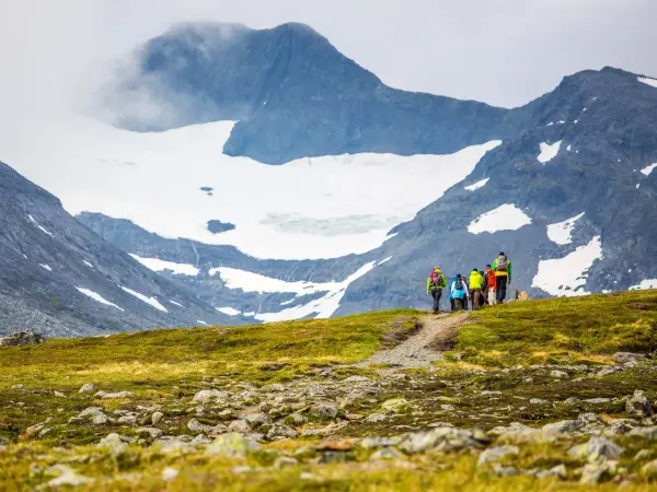 Vandrare med ryggsäckar går längs en stig med glaciärklädda sylarna runt.