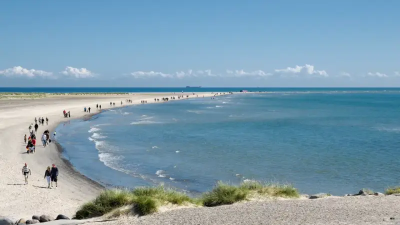En vacker strandpromenad vid Skagen, med folk som njuter av solen och havet. En perfekt resa till Skagen.